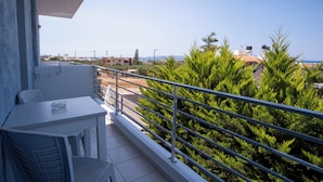 A balcony with a table and chairs, a railing, and a view of trees and buildings. - Ble Island (Hersonissos)