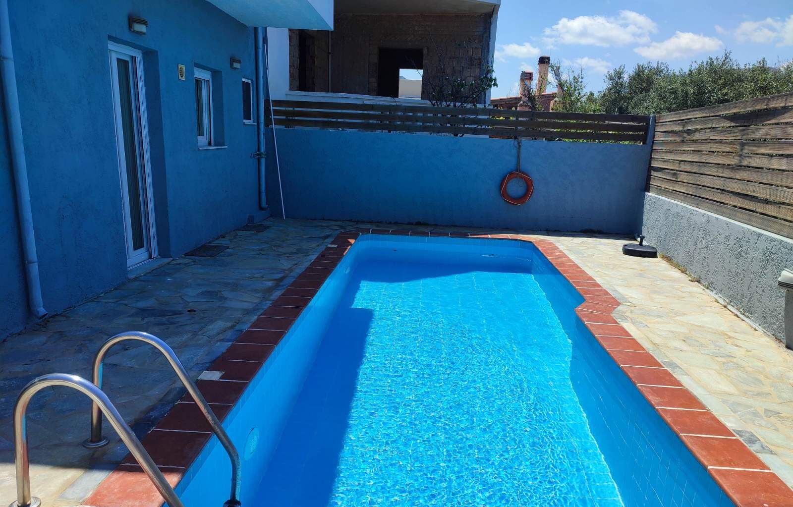 A rectangular swimming pool with a blue interior, surrounded by a tiled deck and a low brick wall.