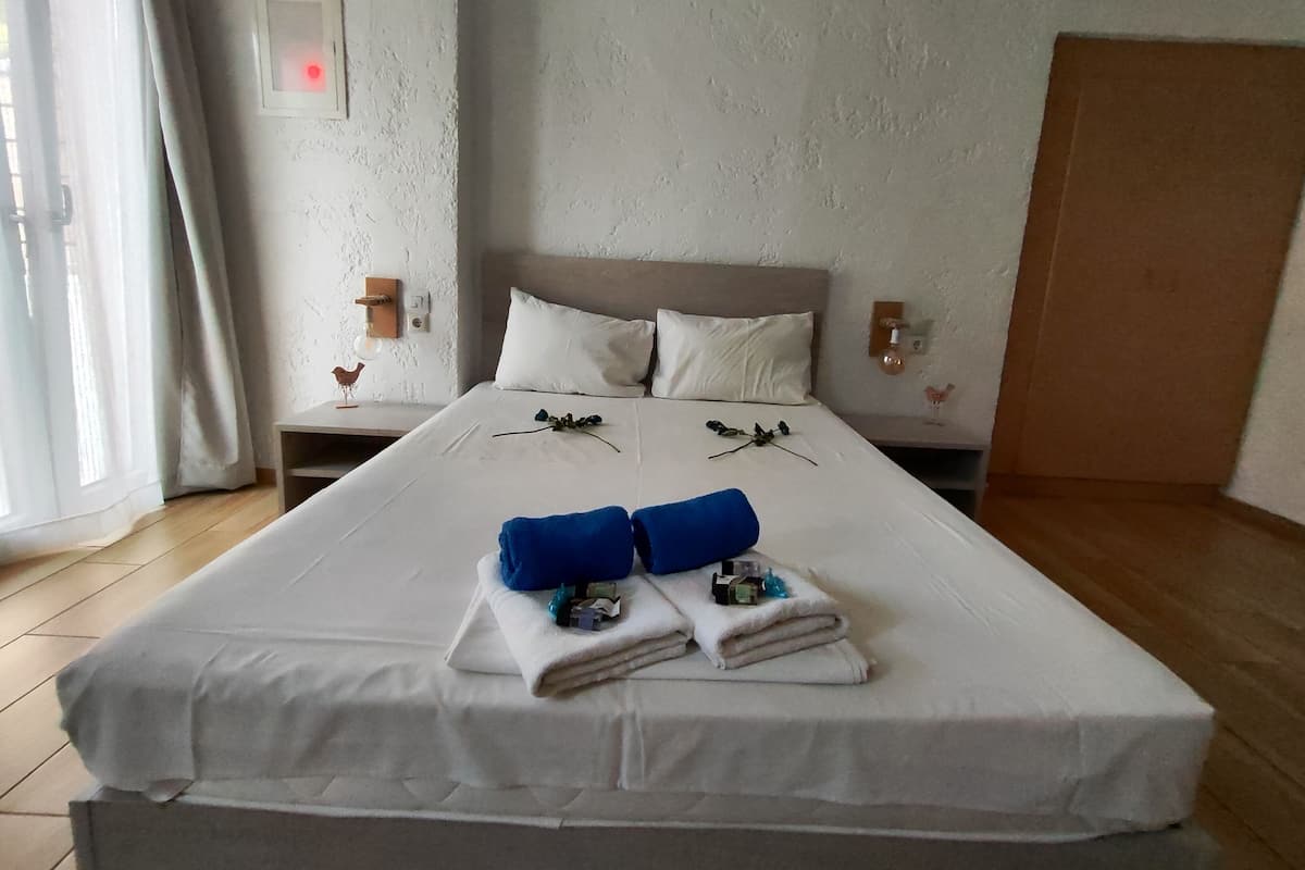 A neatly made bed with white linens, two blue towels, and a decorative branch.