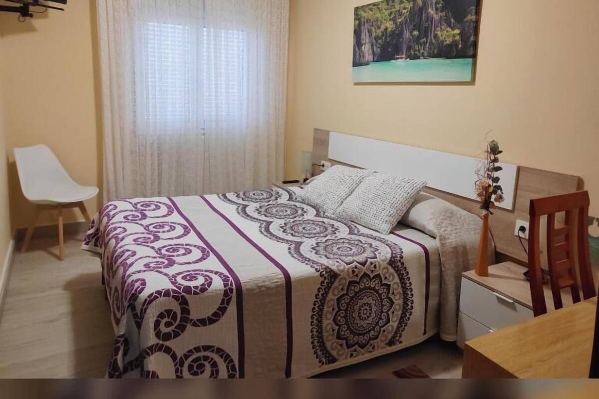 Een slaapkamer met een bed, een bureau, een stoel, een televisie en een schilderij aan de muur.
