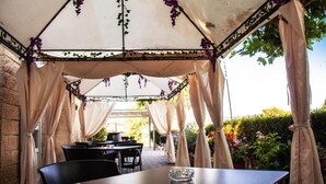 Een terras buiten met een overdekte zithoek, tafels en stoelen.