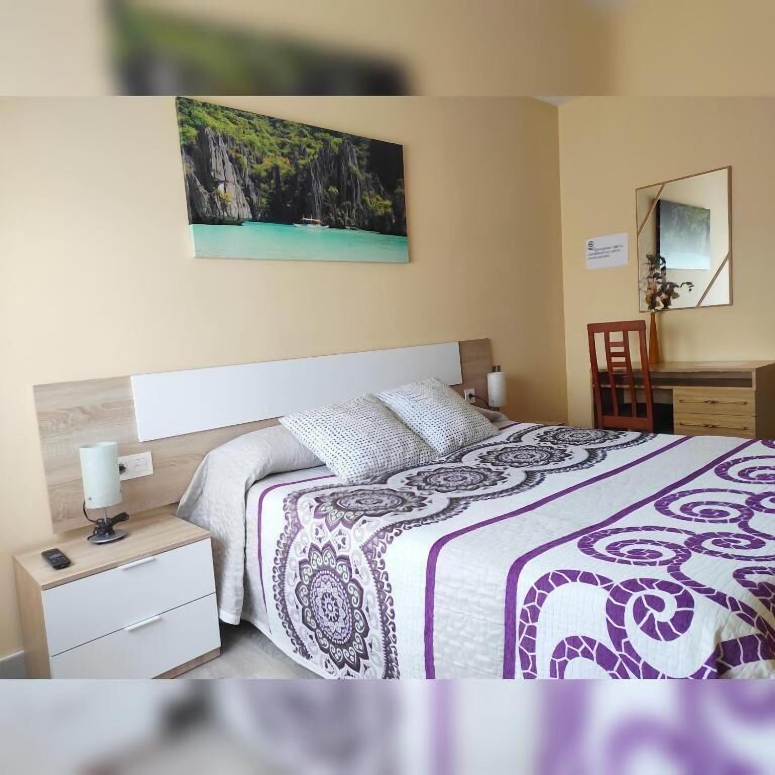 Une chambre à coucher avec un lit, une table de chevet, une chaise, un bureau et un tableau accroché au mur.