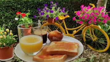 Desayuno con tostadas, un muffin y un vaso de jugo de naranja en un plato, junto a una bicicleta amarilla con cestas de flores.