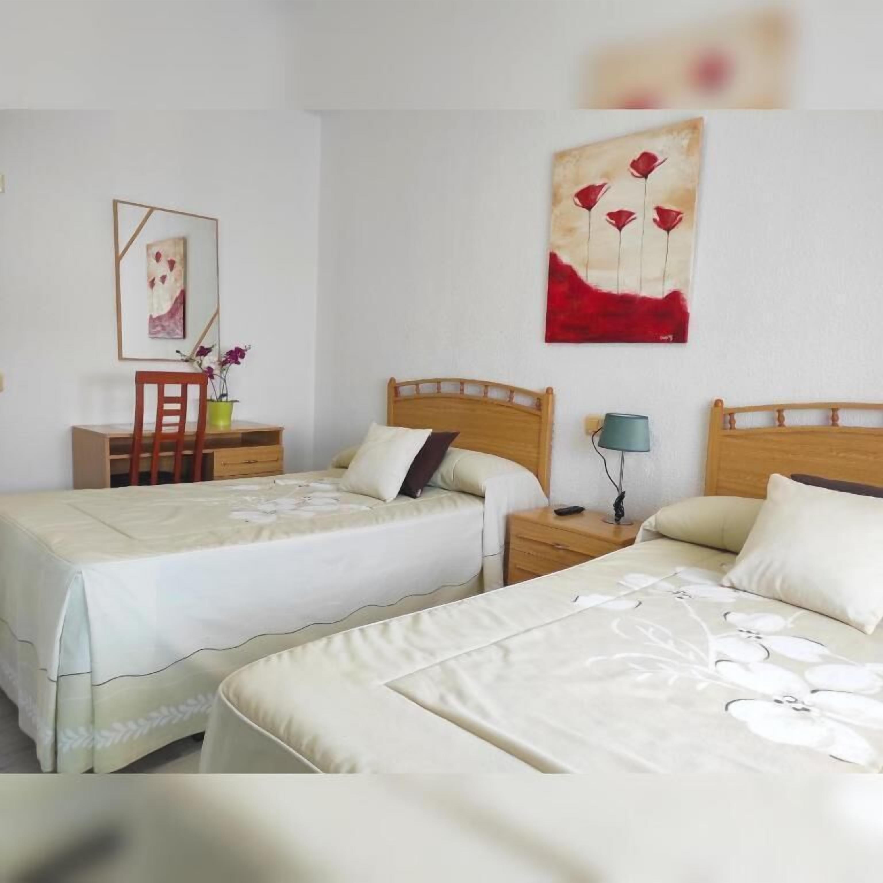 Habitación de hotel con dos camas, un escritorio, una silla, una mesita de noche y una pared con un cuadro.
