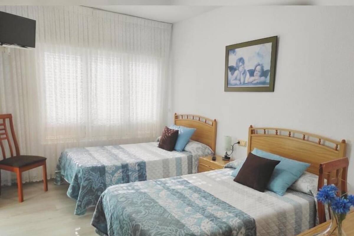 Een hotelkamer met twee eenpersoonsbedden, een houten stoel, een nachtkastje met een lamp en een schilderij aan de muur.