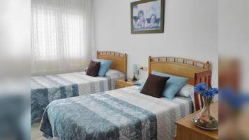 Habitación de hotel con dos camas, una mesita de noche con lámpara, un cuadro en la pared y un florero con flores en la mesita de noche.
