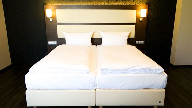 Un lit double avec du linge de lit blanc, une tête de lit en bois et deux lampes de lecture fixées au mur.