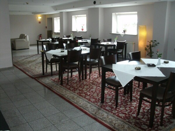 Un área de comedor con varias mesas y sillas, una alfombra estampada y un ventanal que proporciona luz natural.