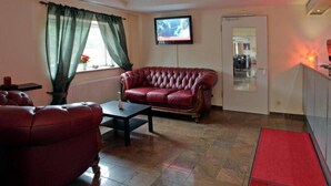 Un salon avec un canapé en cuir rouge, un fauteuil assorti, une table basse, un téléviseur fixé au mur et une porte donnant sur une autre pièce.
