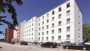 Un hôtel à plusieurs étages, doté d’un design moderne, avec une façade plane ornée de fenêtres régulièrement espacées et une entrée centrale.