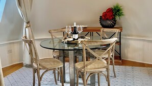 A dining area with a round glass table, four wicker chairs, a vase with red flowers, and a bottle of wine. - Chic Retreat, 2 Queen Beds, FREE PARKING, Walk to Train (Oak Park)
