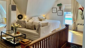 A cozy bedroom with a sloped ceiling, a chandelier, a bed with white linens, a small table with a vase, and a view of the outdoors. - Chic Retreat, 2 Queen Beds, FREE PARKING, Walk to Train (Oak Park)