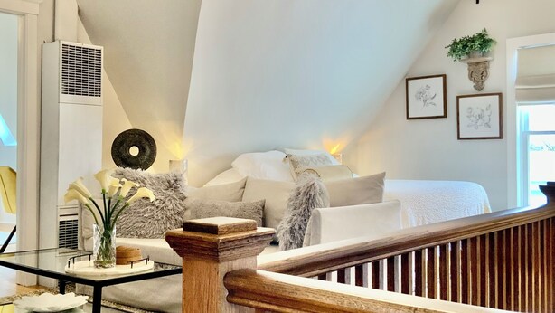 A spacious loft bedroom with a high ceiling, a chandelier, a wooden staircase, and a cozy seating area with a coffee table and decorative items. - Chic Retreat, 2 Queen Beds, FREE PARKING, Walk to Train (Oak Park)