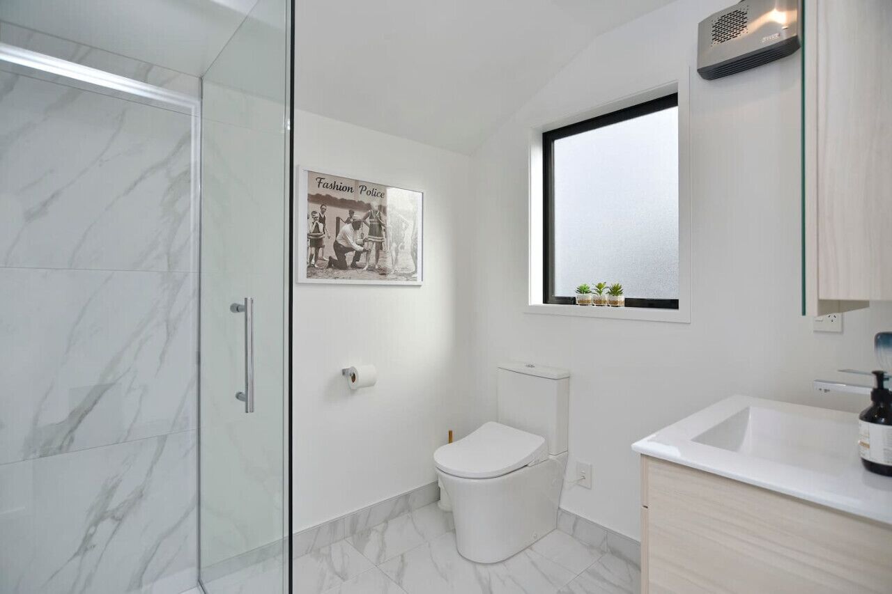 Un bany modern amb una cabina de dutxa de vidre, un vàter, un rentapeus i una finestra sobre el rentapeus.