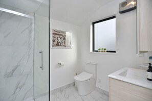 Ein modernes Badezimmer mit Duschkabine aus Glas, Toilette, Waschbecken und Fenster über dem Waschbecken.