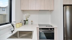 A compact kitchen with a built-in oven, a stainless steel sink, and light wood cabinetry. - Sea Air and Sandy Beach Beautiful 1 bed 1 bath (Christchurch)