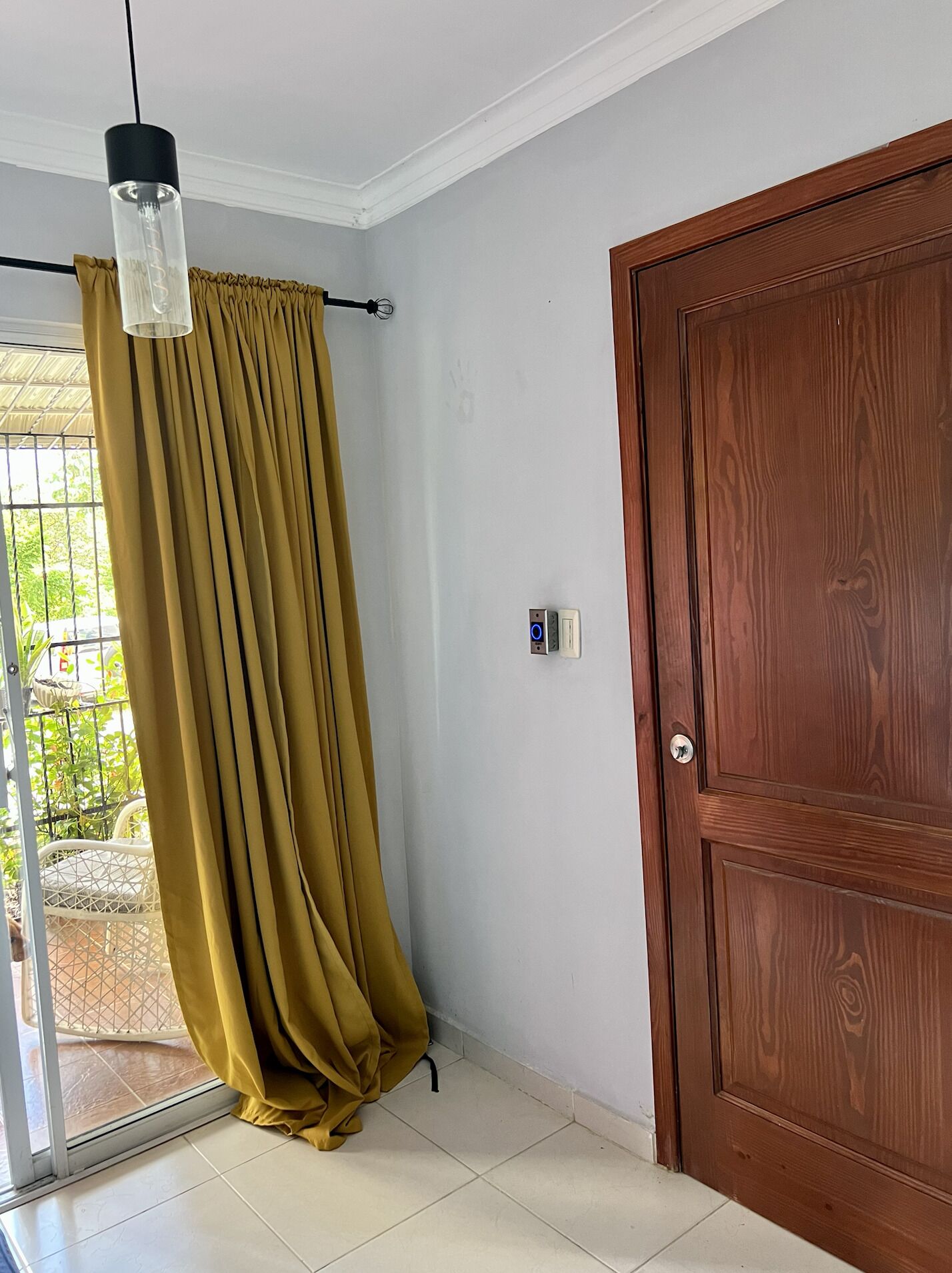 A room with a wooden door, a curtain, a ceiling light, and a tiled floor.