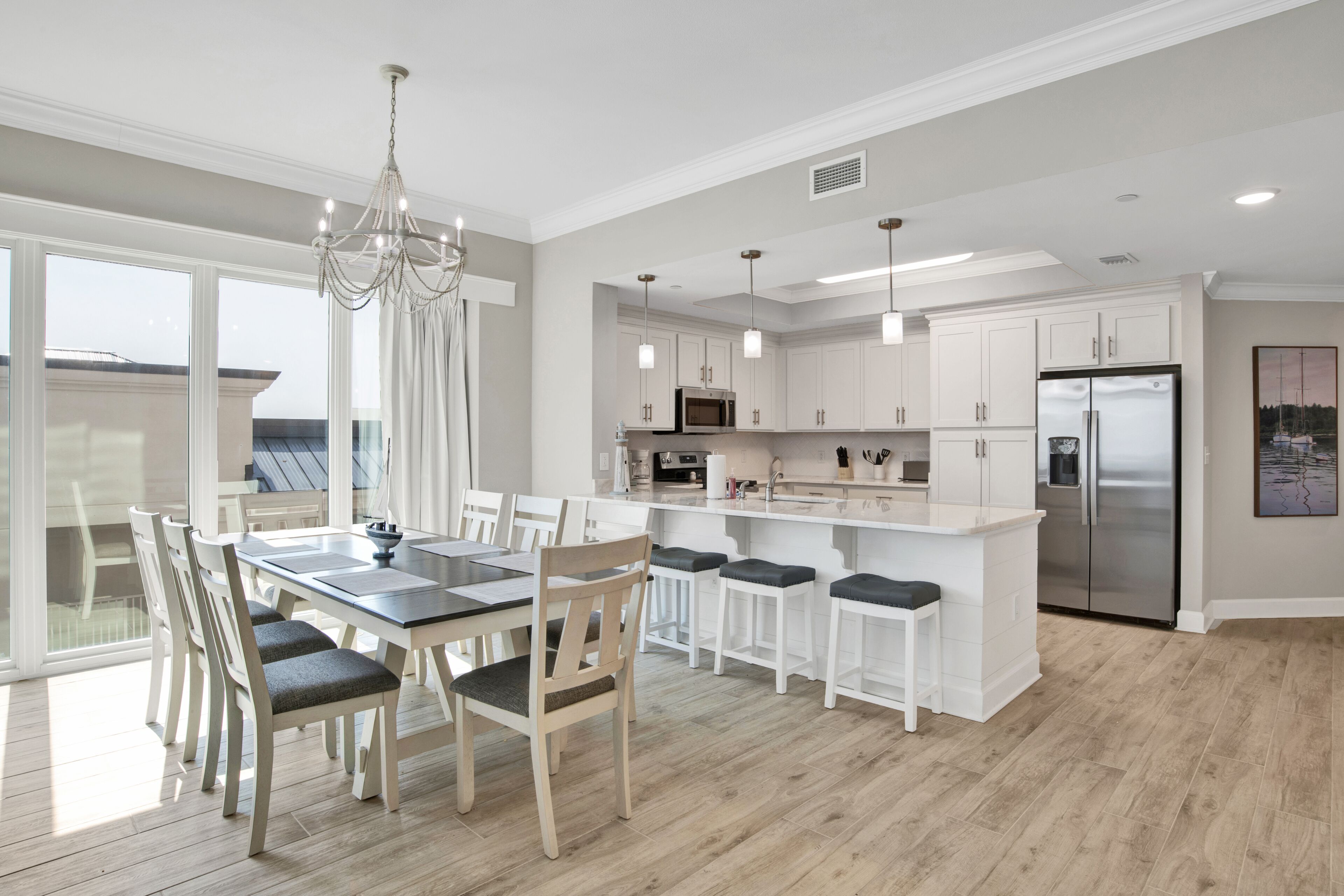 A modern kitchen with white cabinetry, a stainless steel refrigerator, and a dining area with a glass table and chairs.