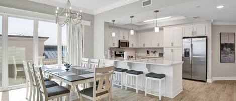 A modern kitchen with white cabinetry, a stainless steel refrigerator, and a dining area with a glass table and chairs.
