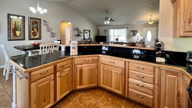 A spacious kitchen with wooden cabinets, a black countertop, and a dining area with white chairs.