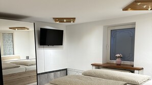 Een moderne slaapkamer met een groot bed, nachtkastjes, een flatscreen televisie en een spiegel.