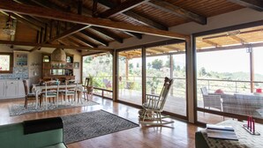 A spacious dining area with a wooden ceiling, large windows offering a view of the outdoors, and a cozy seating area with a rocking chair. - Calypso Villa with Jacuzzi Pool & Sea View (Dafni)