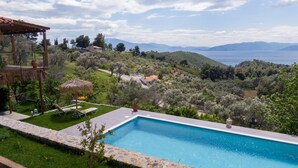 A pool with a view of a mountainous landscape and a thatched-roof structure. - Calypso Villa with Jacuzzi Pool & Sea View (Dafni)