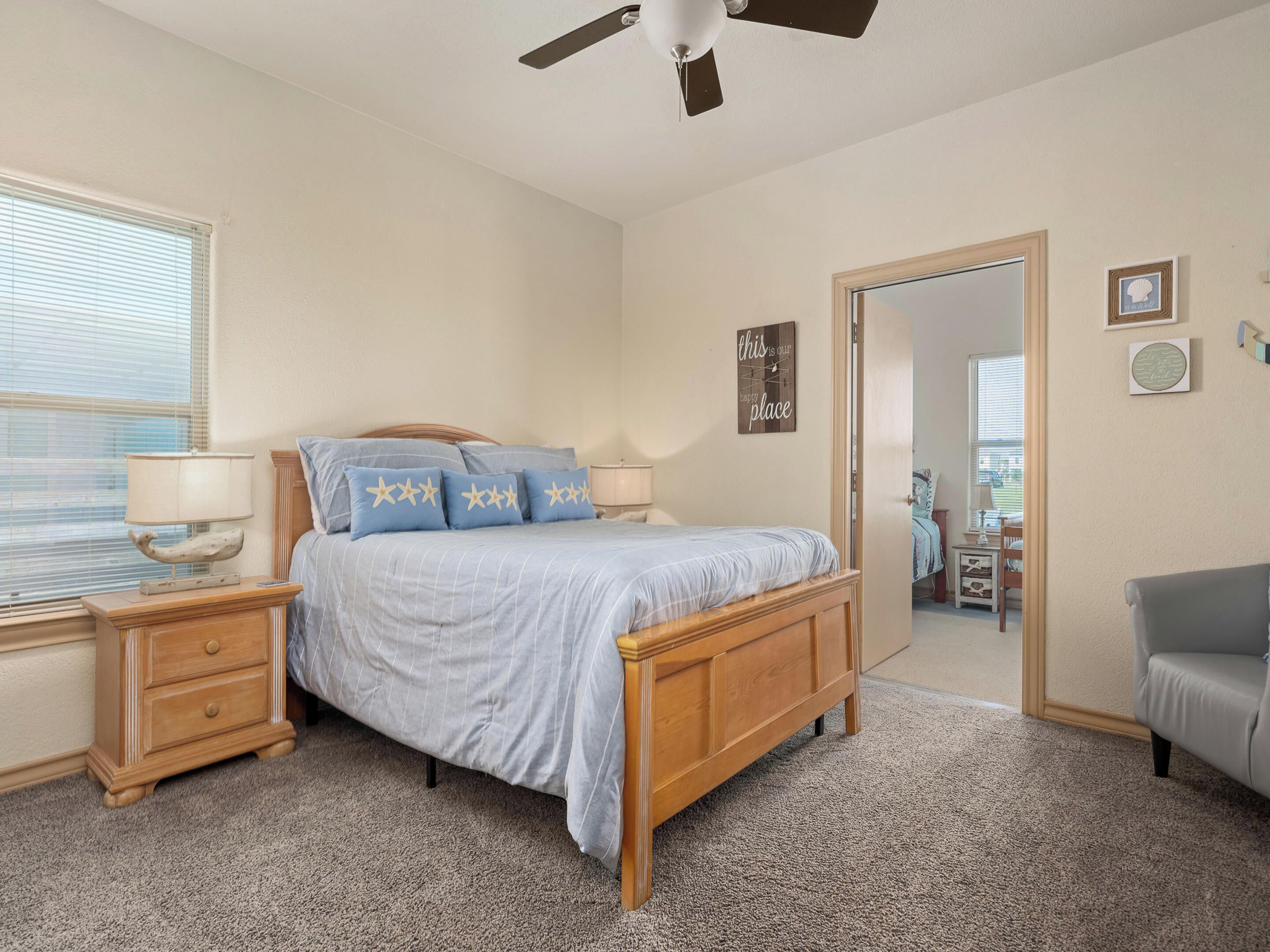 A bedroom with a bed, nightstands, a ceiling fan, and a door leading to another room.