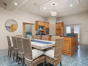 A modern kitchen with wooden cabinets, a central island, and a dining area with wicker chairs and a white table.