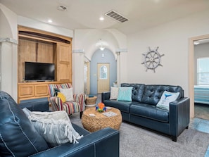 A living room with a TV, two sofas, a coffee table, and a decorative wall piece.