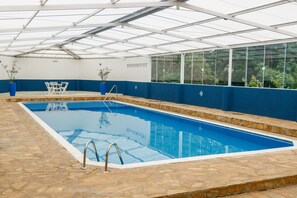 Una piscina techada, una piscina al aire libre, sombrillas