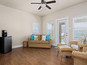 A living room with a brown sofa, two wicker chairs, a coffee maker, and a ceiling fan. - Port Royal Dream by Miss Kitty’s (Aransas Pass)