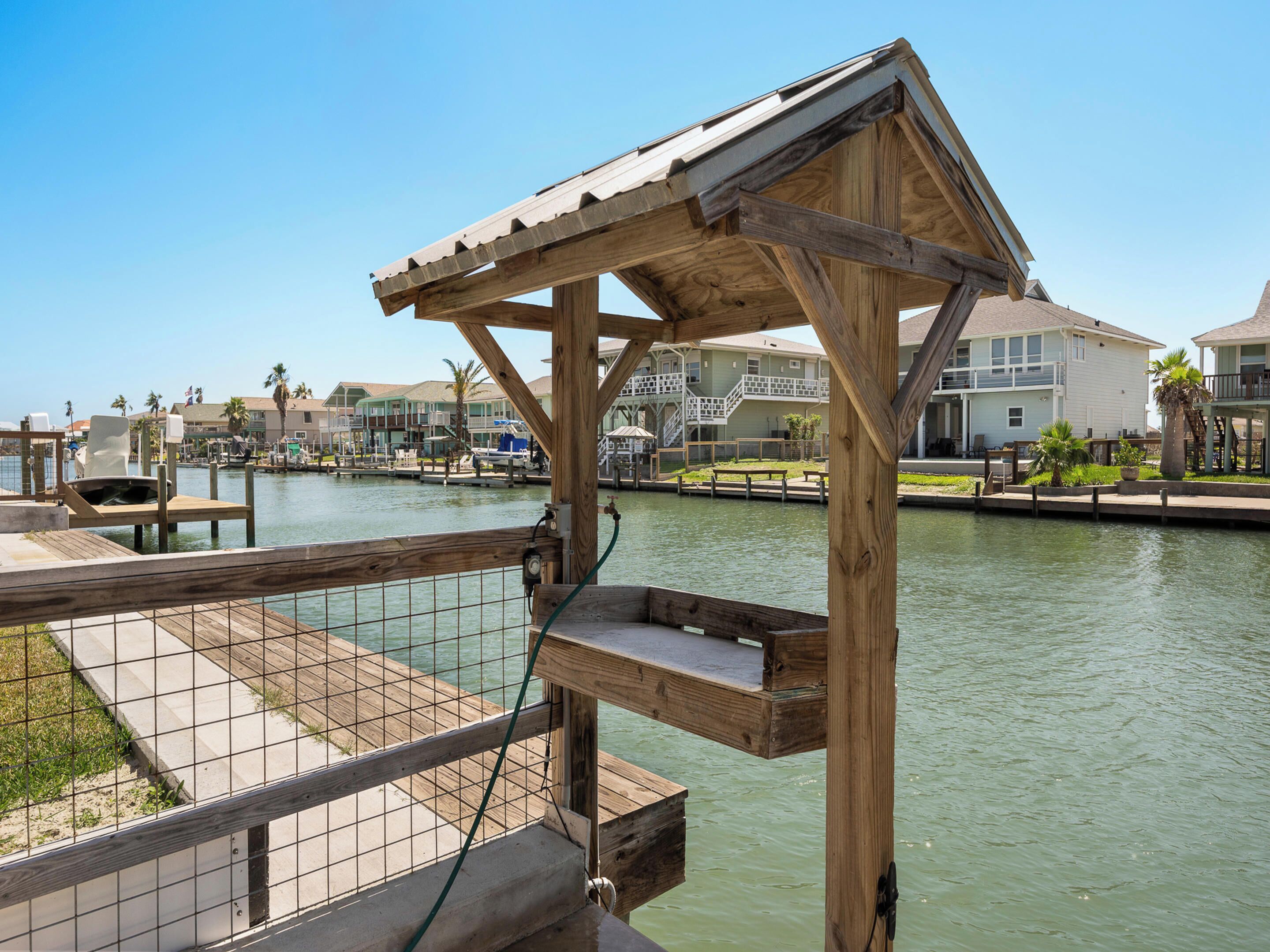 Una terraza de madera con barandilla metálica que da a un puerto deportivo con barcos y casas al fondo.