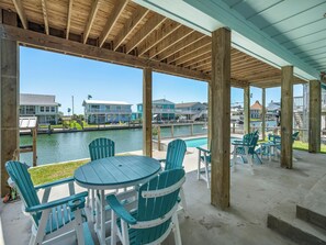 A covered outdoor seating area with a view of a marina and houses. - Port Royal Dream by Miss Kitty’s (Aransas Pass)