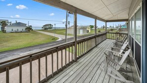 A wooden porch with a view of a grassy area and houses.