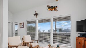 A living room with a wooden coffee table, two chairs, a television, and decorative fish on the wall.
