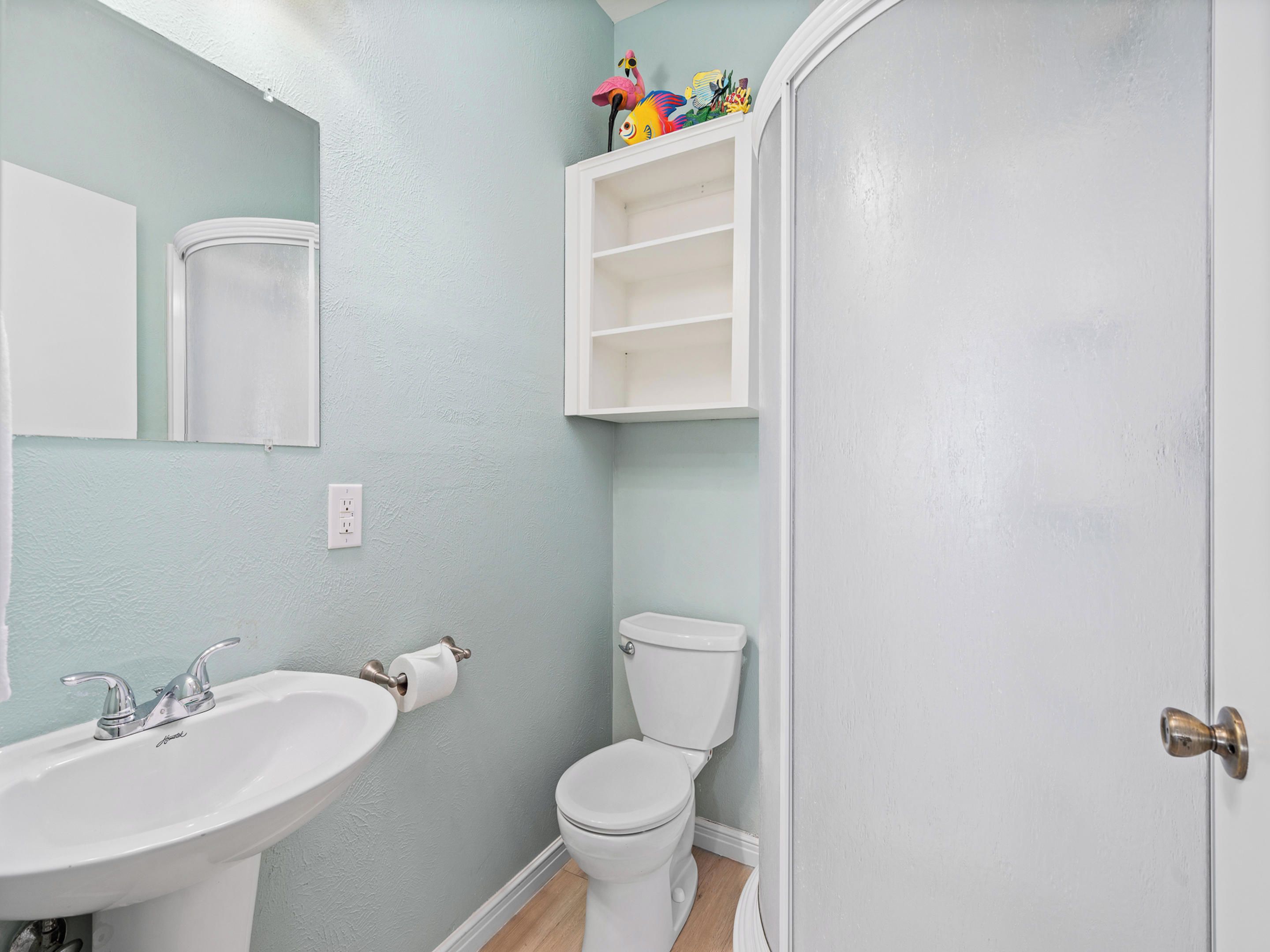 Un baño con lavamanos blanco, inodoro y un armario con objetos decorativos.