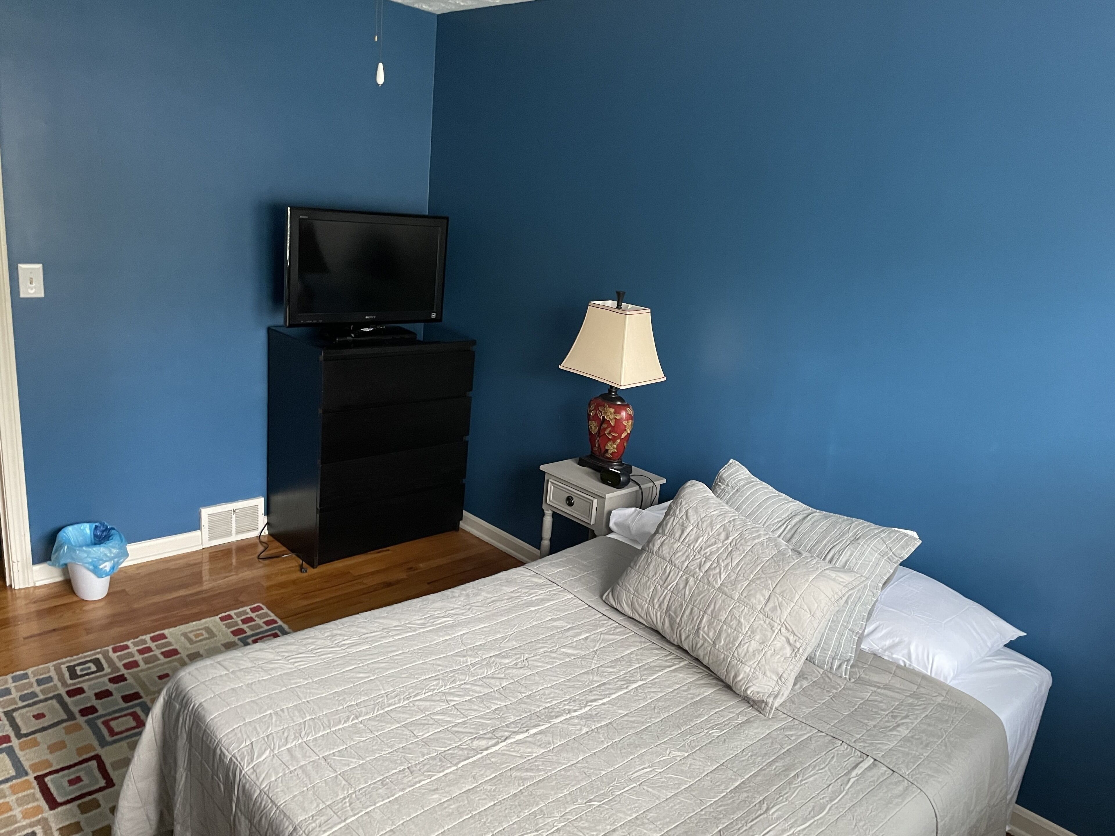Una camera da letto con un letto, una TV su una cassettiera, una lampada e un parete blu.
