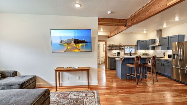 A modern kitchen with wooden beams, a dining area with a rug, and a large island. - The Mountain Ave House by WanderLodges (Ashland)
