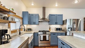 A modern kitchen with blue cabinets, stainless steel appliances, a built-in oven, and a microwave. - The Mountain Ave House by WanderLodges (Ashland)