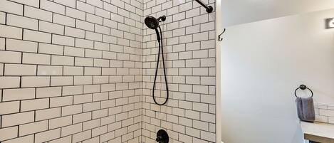 A bathroom with white tiled walls, a shower with a black hose, and a toilet.