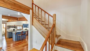 A wooden staircase leading to a kitchen with a central island and bar stools. - The Mountain Ave House by WanderLodges (Ashland)