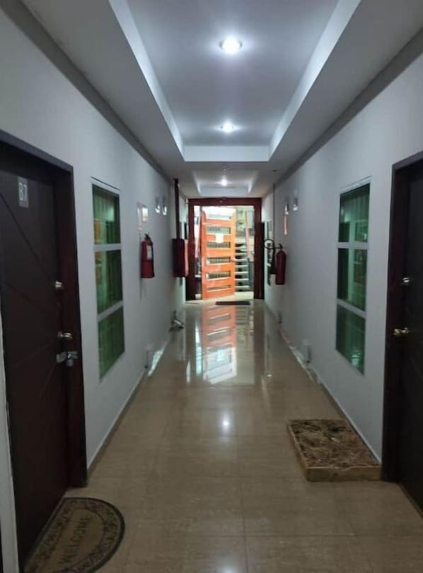 A hallway with a tiled floor, doors on both sides, and a view into a room with a window and a door at the end.