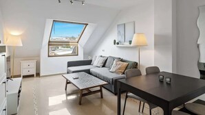 A modern living room with a sofa, coffee table, and dining table. There is a skylight window and a lamp on each side of the room. - Stunning Rooftop Condo with Sea Views in Fuengirola (Fuengirola)
