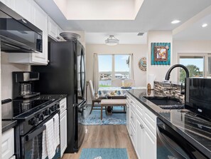 A modern kitchen with black appliances, a dining area with a view, and a decorative wall piece. - Gaetano's Getaway by Miss Kitty’s (Rockport)