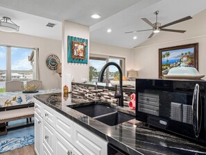 A modern kitchen with a black countertop, white cabinets, a large window, and a view of the sea. - Gaetano's Getaway by Miss Kitty’s (Rockport)