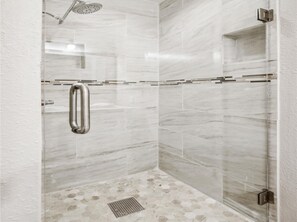 A modern shower with a glass door, a rain showerhead, and a handrail. - Beachside Pearl by Ryson Vacation Rentals (Galveston)