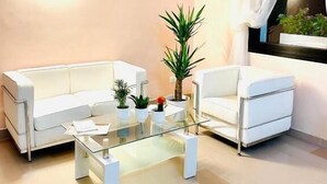 Un salon moderne avec deux canapés blancs, une table basse en verre et plusieurs plantes en pot.