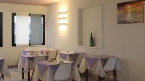 Un espace repas avec des tables dressées pour quatre personnes, chacune étant agrémentée de chaises blanches et de nappes violettes.