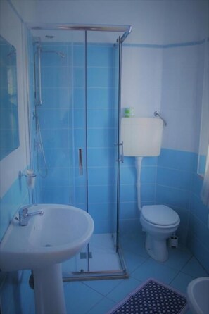 A bathroom with a glass shower enclosure, a white sink, and a toilet. - Adria Nuova (Rimini)